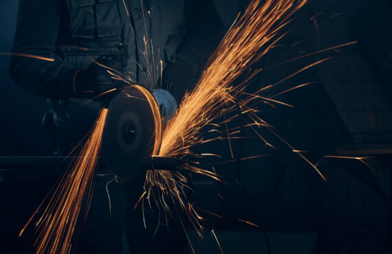 Worker polishing metal with special equipment in dark room.